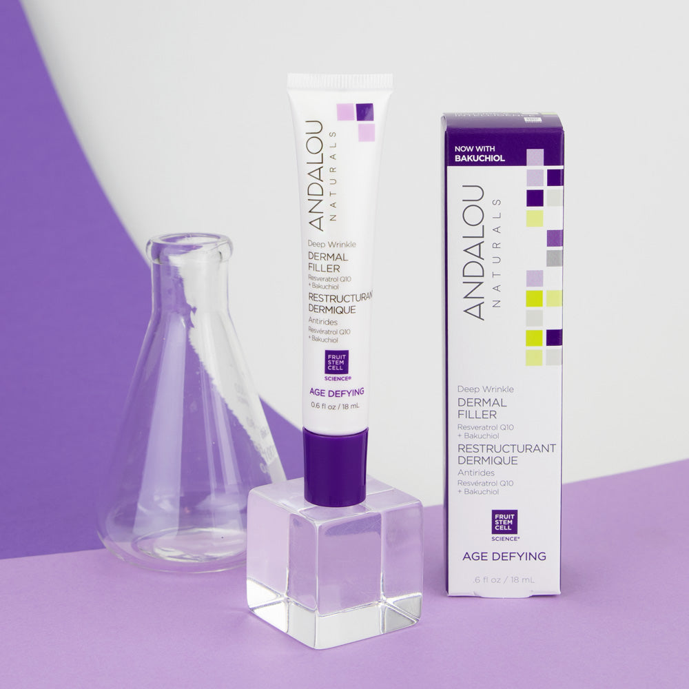 An Andalou Naturals Deep Wrinkle Dermal Filler tube with its packaging displayed against a purple background, featuring a beaker as a prop.
